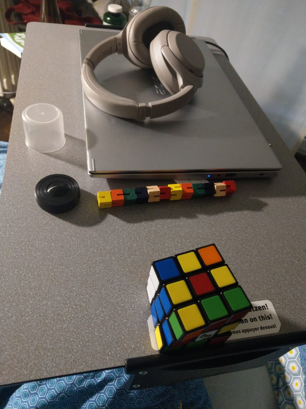 Bild vom Nachttisch am Krankenhaus. Darauf ein Laptop, Active Noise Canceling Kopfhörer, Stim Toys und ein Rubic's Cube.
